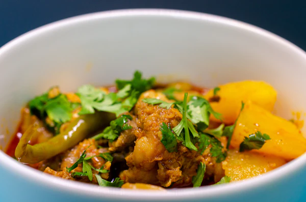 Close up of chicken and potato salan with green chilli and coriander in a white bowl.