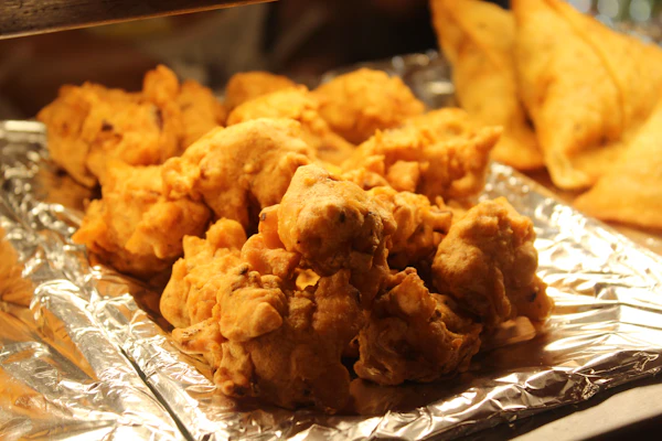 Crispy fried chicken broast pieces on foil, samosas in the background.