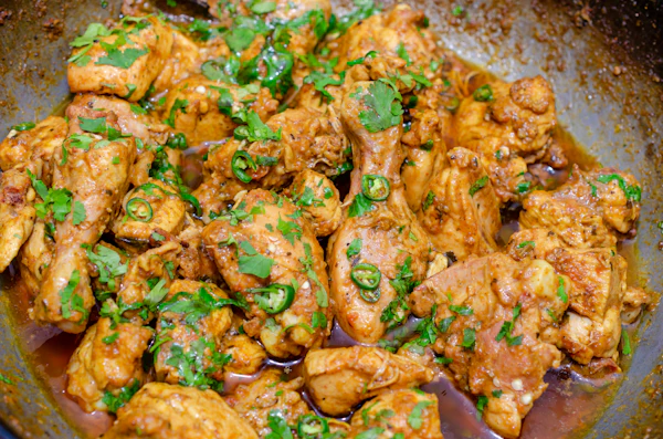 Chicken karahi in a dark pan, topped with green chillies and fresh coriander.