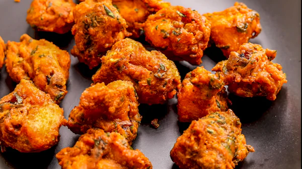 A pile of crisp golden chicken pakoray on a dark plate.