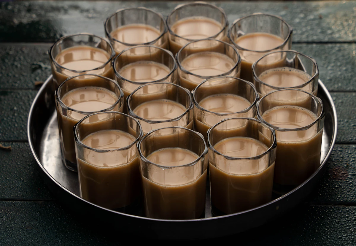 Small glasses of milky doodh patti chai on a round steel tray.